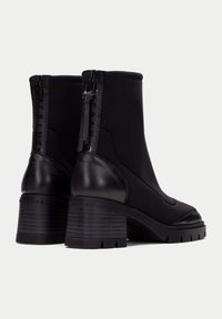 Botas negras de tobillo con un diseño elegante, que presentan un panel trasero de cuero texturizado y un frente de tela elástica. Tacones gruesos y estriados, además de cremalleras laterales.