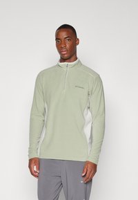 Pull en polaire vert clair avec une fermeture éclair quart, des panneaux latéraux blancs contrastants et un logo Columbia sur la poitrine. Texture lisse.