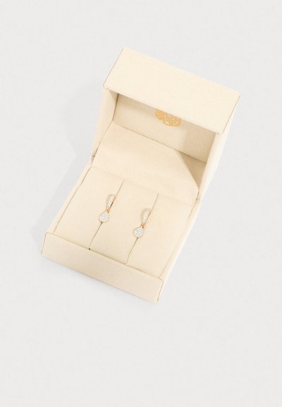 Rozā zelta auskari ar asaras formas dizainu, ar teksturētu apaļu akcentu, izstādīti bēša samta iekšpusē.