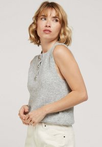 Débardeur gris en laine sans manches avec un col rond, orné de trois boutons décoratifs et d'une texture douce, associé à un pantalon de couleur claire.
