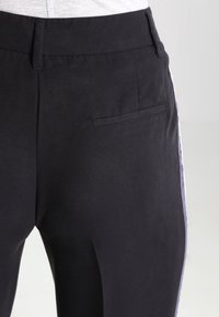 Black trousers with a smooth texture, featuring a back pocket and side stripe detail in a contrasting color. Tailored fit and clean lines.