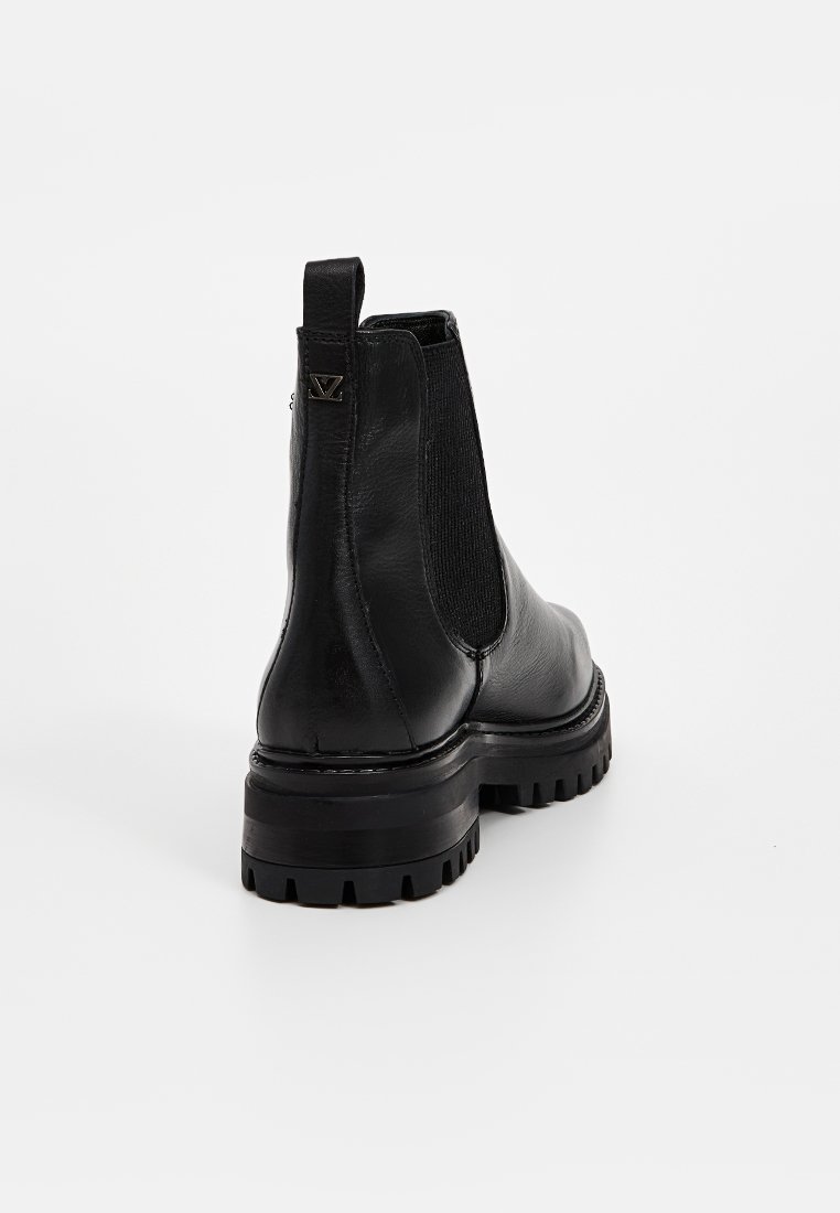 Bottines en cuir noir avec un panneau latéral élastique texturé, semelle en caoutchouc épaisse et languette à l'arrière. Caractéristiques de design minimaliste.