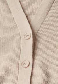 Helle beige Strickjacke mit geripptem Muster, mit V-Ausschnitt und zwei Kunststoffknöpfen vorne. Weiches Strickmaterial.