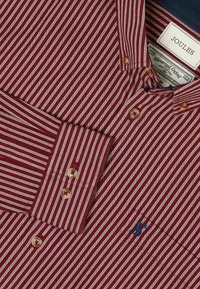 Rød- og hvidstribet skjorte i merceriseret Oxford-bomuld med navyblå krave, brune knapper og et lille blåt logo på brystet.