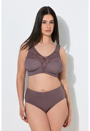 Donna che indossa un reggiseno lilla a pois con dettagli in pizzo e mutandine a vita alta abbinate, in piedi su sfondo bianco.