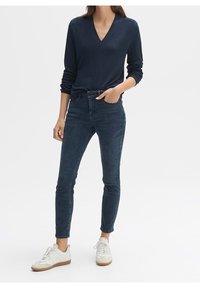 Námořnický svetr s výstřihem do V, slim-fit tmavé džíny, bílé tenisky s béžovými akcenty a texturovanou podrá žkou. Jednoduchý design, casual styl.