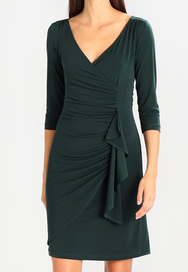 Robe vert foncé jusqu'au genou avec encolure en V et manches trois-quarts. Présente un effet froncé et un accent à volants sur le côté. Tissu à texture douce.