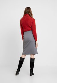 Un pull rouge en peluche et court avec une jupe grise d'une longueur jusqu'aux genoux. Des bottes noires à talons hauts et montantes. Fond simple, focalisation sur les détails de la tenue.