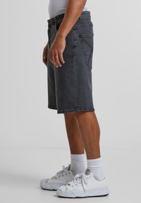 Schwarze Denim-Shorts mit geradem Schnitt, vorderen Taschen und einem auffälligen Design der Gesäßtasche. Kombiniert mit weißen Sneakern und Crew-Socken.