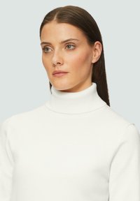 Pull encolure roulée blanc au design ajusté et col côtelé. Texture douce et tissu lisse avec des manches longues. Style minimaliste.