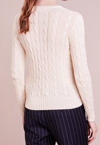 Krämfärgad stickad tröja med kabelmönster, långa ärmar och rundad halsringning. Kombinerad med marinblå randiga byxor.