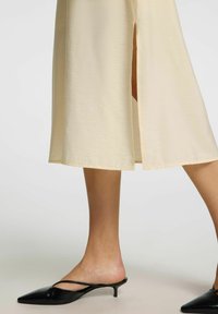 Beige midi sukně s bočním rozparkem, vyrobená z hladkého a lehkého materiálu. V kombinaci s černými lodičkami s špičatou špičkou.