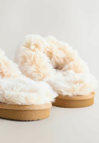 Faux pels slippers med en blød hvid overdel, tan suede-lignende sål og rund form. Har en tyk, fluffy tekstur og sømløs konstruktion.
