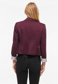 Blazer bordeaux court à manches longues, avec poignets rayés. Tissu lisse avec une silhouette ajustée et un col cranté.