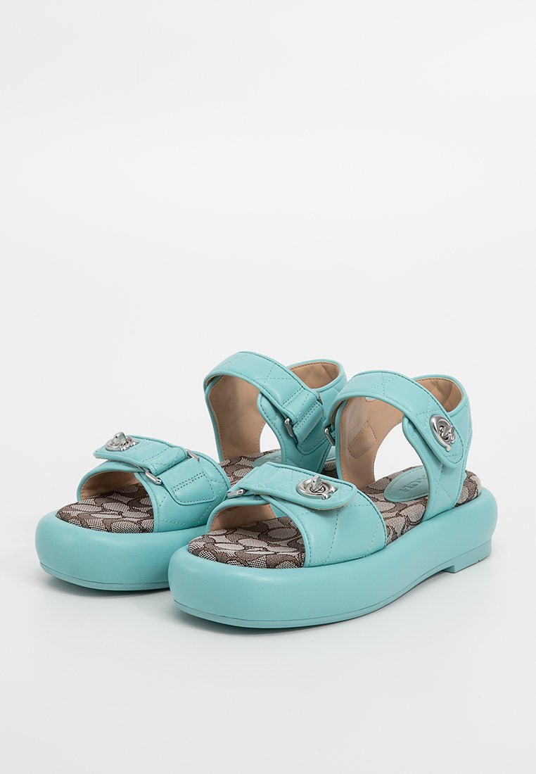 Turkusowe sandały z regulowanymi paskami, metalowymi klamrami i teksturowanymi wkładkami z subtelnym wzorem. Płaska podeszwa.