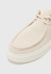 Scarpa in suede beige dal design minimalista, con punta arrotondata, cuciture a vista e suola in gomma bianca. I lacci sono integrati sopra il vamp.
