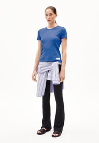 Blauw fitted ribbed t-shirt, gelaagd met een gestreepte lichtblauwe blouse geknoopt om de taille, gecombineerd met zwarte flare-broeken en donkere sandalen.