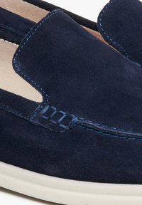 Granatowe zamszowe buty wsuwane z kontrastującym niebieskim przeszyciem i fakturowanym wierzchem. Posiadają wycięty wzór oraz białą gumową podeszwę.