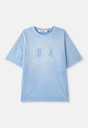 Camiseta de algodón azul claro con mangas cortas y cuello redondo. Presenta el texto bordado "IBIZA" en un azul ligeramente más oscuro. Textura suave.