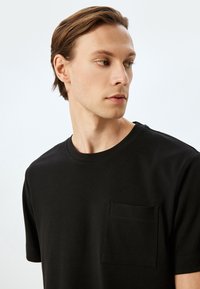 Zwart T-shirt met korte mouwen van katoen, voorzien van een borstzak met bijpassende stiksel en een ronde hals. Gladde textuur.