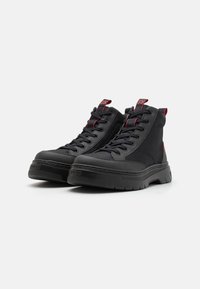 Zapatillas altas negras que presentan una combinación de materiales suaves y de malla, detalles en rojo, cordones redondos y una suela de goma gruesa.