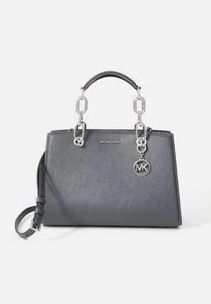 Szara torebka Michael Kors z srebrnymi łańcuszkowymi uchwytami, regulowanym paskiem na ramię i zawieszką z logo MK na jednolitym białym tle.