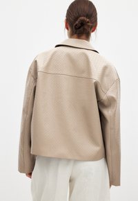 Beige vävd läderjacka med en strukturerad krage, med en texturerad yta och rak passform, i kombination med vita byxor.