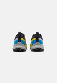 Scarpe sportive con tomaia nera, dettagli blu e gialli, tacco texturizzato e suola grigia con un battistrada decorato.