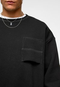 Zwarte sweatshirt met een voorkussen met witte stiksels, ronde halslijn en een zachte textuur. Geschikt voor casual draag.