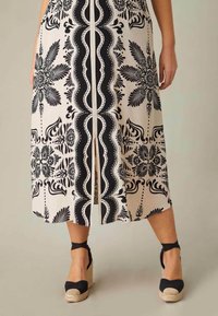 Musta-valkoinen kuviollinen midi-mekko, jossa on etuläppä ja kukkakuosiset yksityiskohdat. Yhdistetty mustiin espadrille-korkokenkiin, joissa on nilkkavöitä.