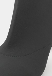 Stivaletto nero realizzato in tessuto elasticizzato con una texture liscia, caratterizzato da una forma curva e dettagli di cucitura discreti.