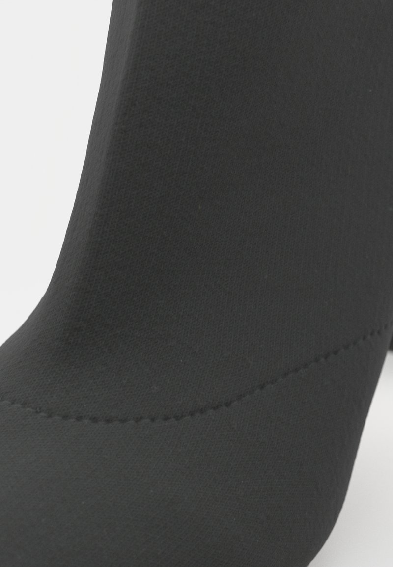 Schwarzer Knöchelstiefel aus Stretchstoff mit glatter Textur, der eine geschwungene Form und dezente Nahtdetails aufweist.