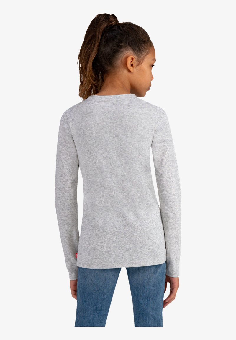 Camisa gris de manga larga con cuello redondo y dobladillo recto, hecha de una tela suave y texturizada, combinada con jeans de mezclilla azul.