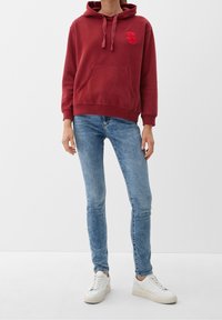 Sweat à capuche bordeaux avec capuche à cordon, poche avant et logo brodé. Associé à un jean bleu clair et des baskets blanches.