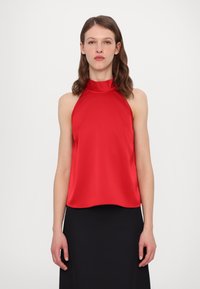 Top rouge à col halter en tissu lisse, présentant une coupe décontractée, un ourlet incurvé et un design minimaliste. Associe à une jupe noire.