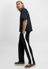 Marineblå short-sleeve t-shirt parret med sorte bukser med en hvid side-stribe. Modellen bærer brune sneakers med en tekstureret overflade.