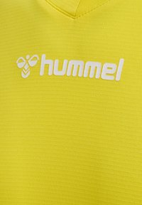 Gelbes Sportoberteil aus strukturiertem Stoff, mit einem weißen Logo einer stilisierten Biene und dem markanten Markennamen "hummel".