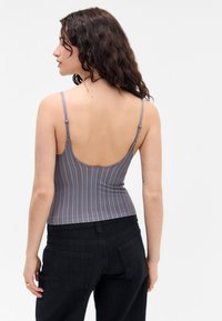 Gray striped tank top with thin adjustable straps, fitted design, smooth texture, and a low back, paired with black textured pants.