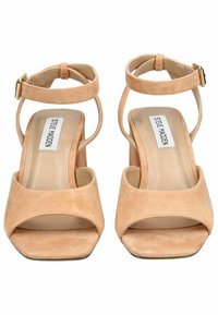 Sandalias de tacón alto de ante beige con punta abierta cuadrada, tira en el tobillo y detalle de hebilla dorada. Presentan una parte superior texturizada y una plantilla suave.