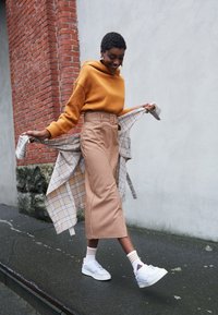 Brun huvtröja, rutiga kjol, lager på lager rutig jacka. Vita platåskor och randiga strumpor fulländar stilen. Urban gatumiljö.