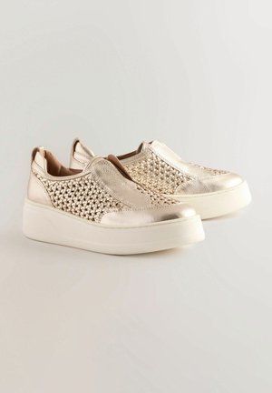 Zapatos slip-on metálicos dorados presentan una textura trenzada en la parte superior, un acabado suave y una suela de plataforma blanca, ofreciendo un diseño moderno.