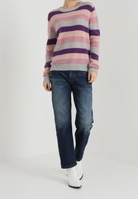 Pasiasty sweter w odcieniach różu, szarości i fioletu, wykonany z miękkiego materiału, zestawiony z ciemnoniebieskimi dżinsami i białymi botkami za kostkę.