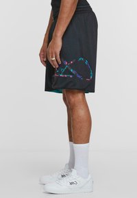 Svart mesh idrettsshorts med et fargerikt mønster og logo; elastisk midje; sammen med hvite joggesko og crew-sokker.