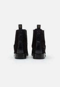 Bottines en suède noir avec détails en cuir brillant, bout légèrement arrondi et talon bas. Présente des languettes de tirage avec logo à l'arrière.