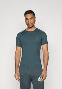 T-shirt de sport à manches courtes en bleu sarcelle foncé, avec un col rond et une coupe ajustée. Présente le logo Nike Pro en noir sur la poitrine.