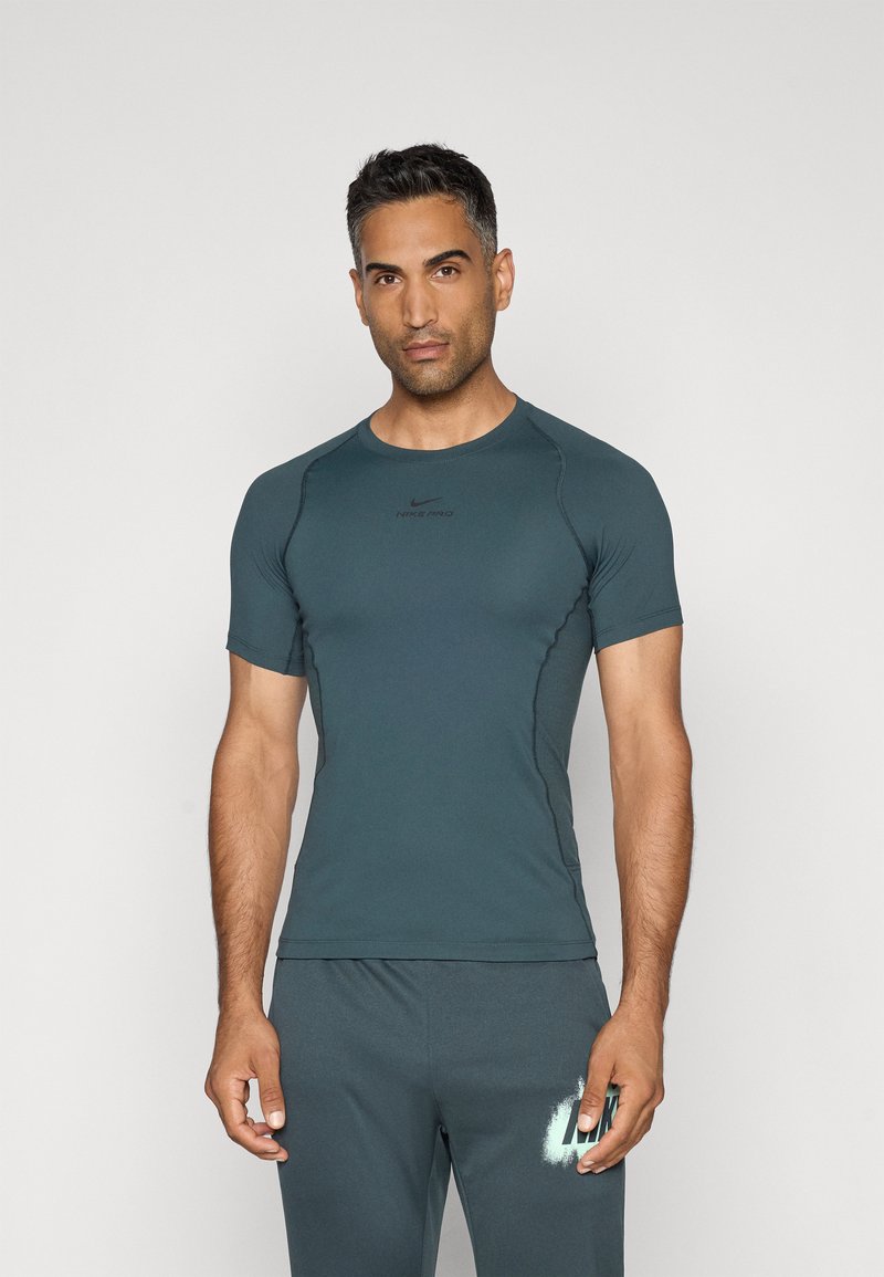 T-shirt de sport à manches courtes en bleu sarcelle foncé, avec un col rond et une coupe ajustée. Présente le logo Nike Pro en noir sur la poitrine.