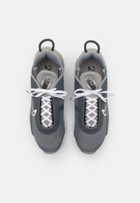 Scarpe sportive grigie con tomaia in tessuto a rete, punta arrotondata, lacci bianchi e linguette per il tallone. Presentano un design in contrasto tra nero e grigio.