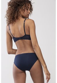 Rintaliivi tummansinisen pitsireunuksella, jossa on säädettävät hihnat ja takakiinnitys, yhdistettynä sileään, vastaavaan bikinitoppihousuun. Pehmeä kangastuntu.