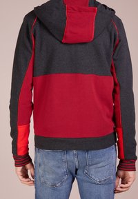 Felpa con cappuccio caratterizzata da un design a blocchi di colore con sezioni grigio scuro e rosse; realizzata in un morbido tessuto con dettagli a coste.