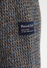 Material tricotat maro și albastru cu o pată bleumarin pe care este inscripționat "Petrol Ind, Denim Driven, Ref. 5026 Since '89 U.S.A."